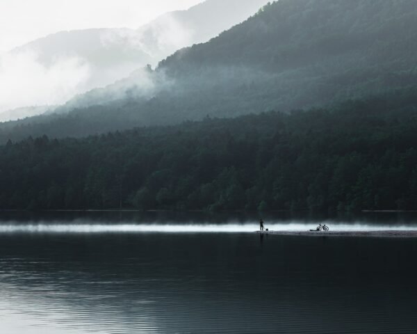 A man with a bicycle in a fog near a lake