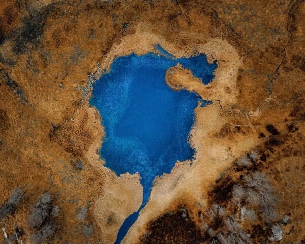 An aerial photograph of a blue lake with an interesting shape surrounded by yellow lands